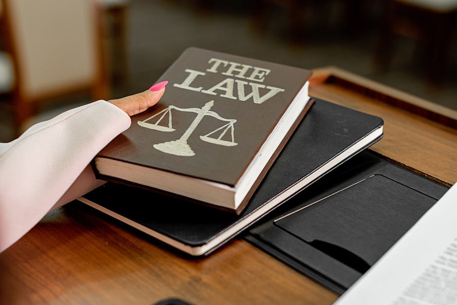 Closeup image of a law book titled 'The Law' on a wooden desk with scales of justice